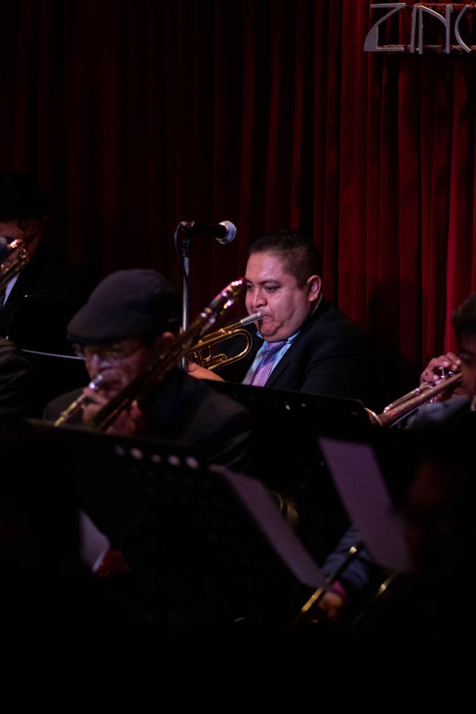 Músicos de jazz tocan trompetas en una actuación en vivo en un local con poca luz.